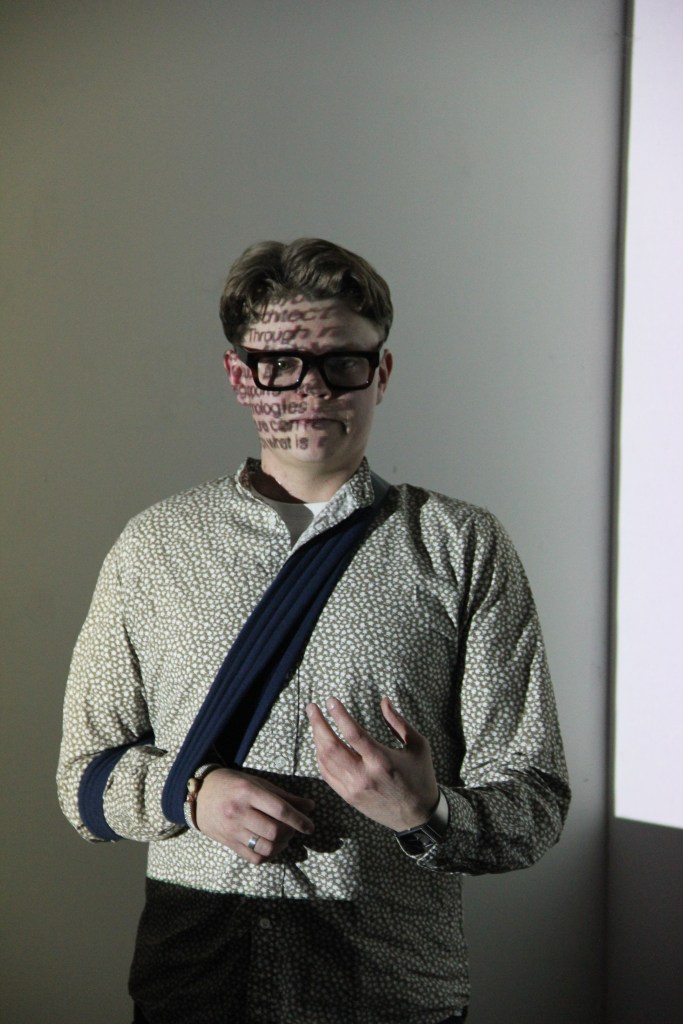 Kalle Bexelius stands in front of a projection during his presentation so that letters are projected onto his face